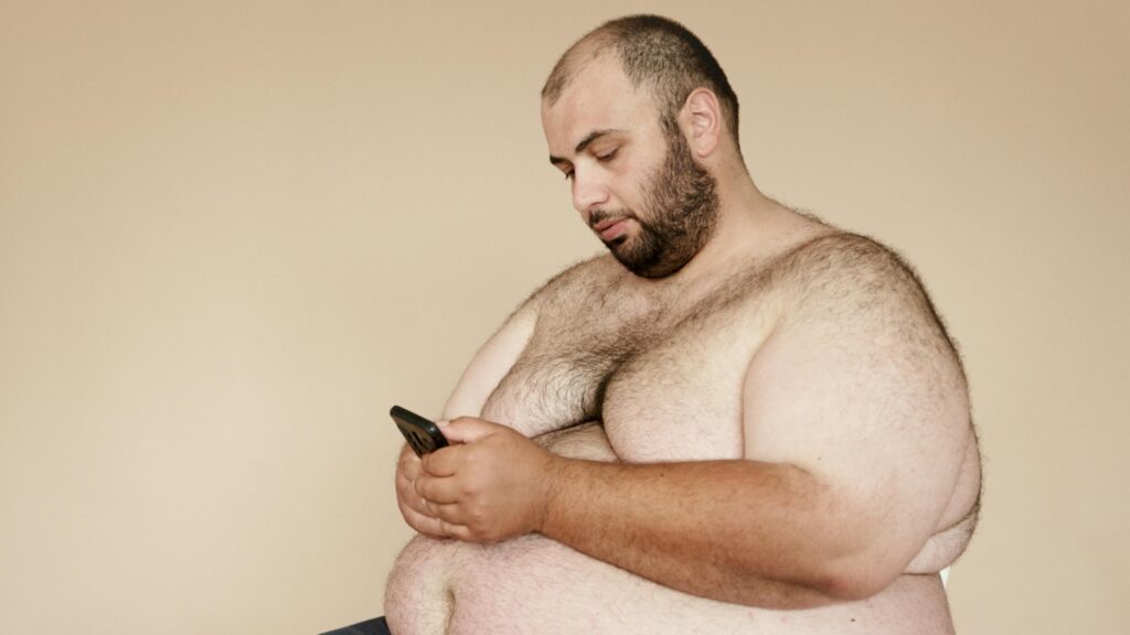 Plus-size bearded man sitting and using smartphone. Focus on lifestyle and technology in a relaxed setting.